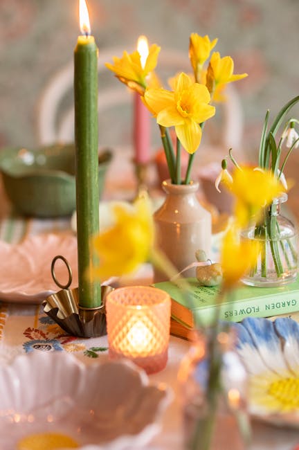A glass vase wrapped in light brown paper and tied with a rustic string holding a vibrant bouquet of fresh tulips in pastel pink, yellow, deep red, and white, with lush green leaves and stems. The arr